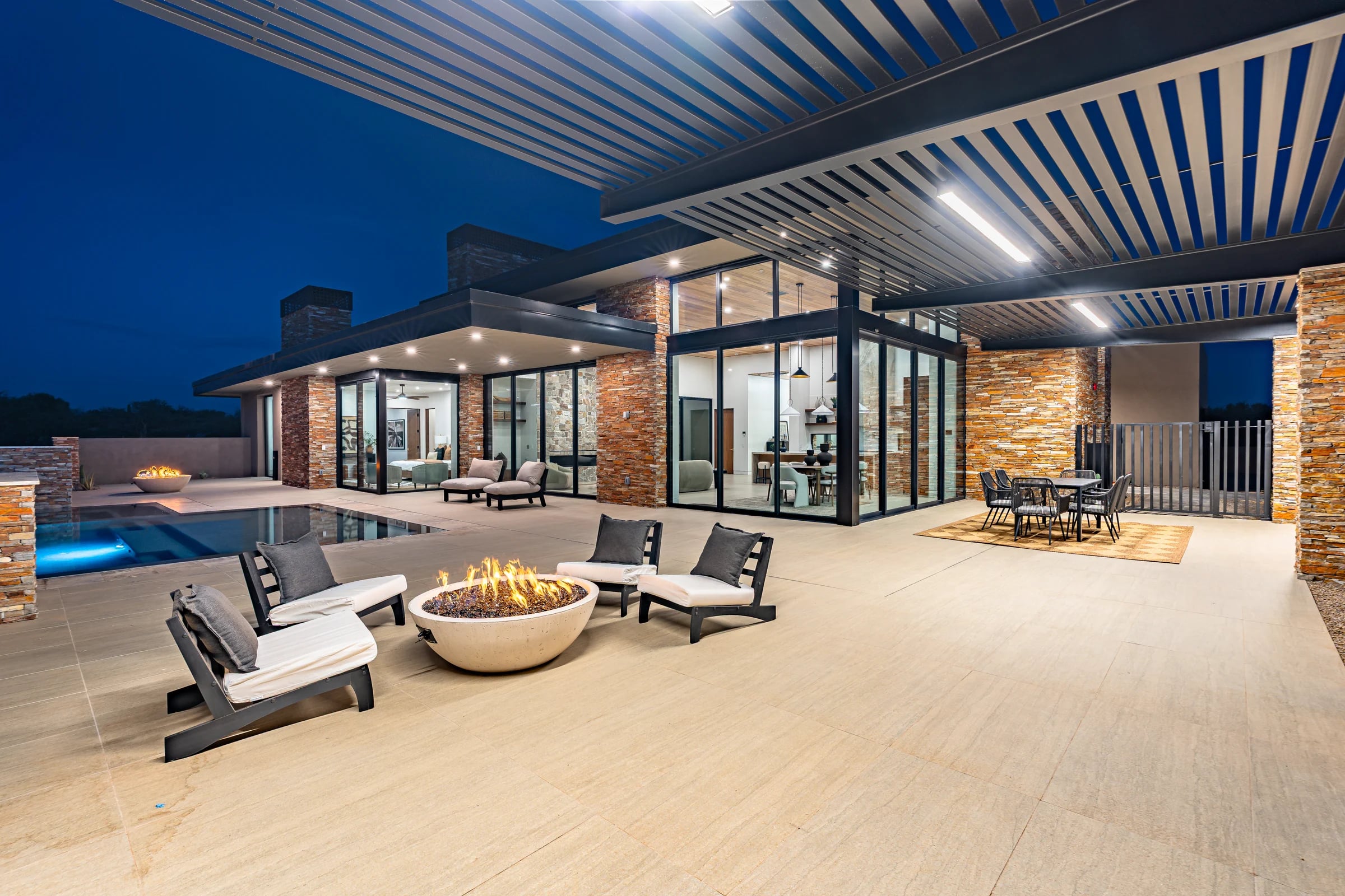 Stone columns and a steel pergola frame the illuminated terrace and pool at the Salero residence.